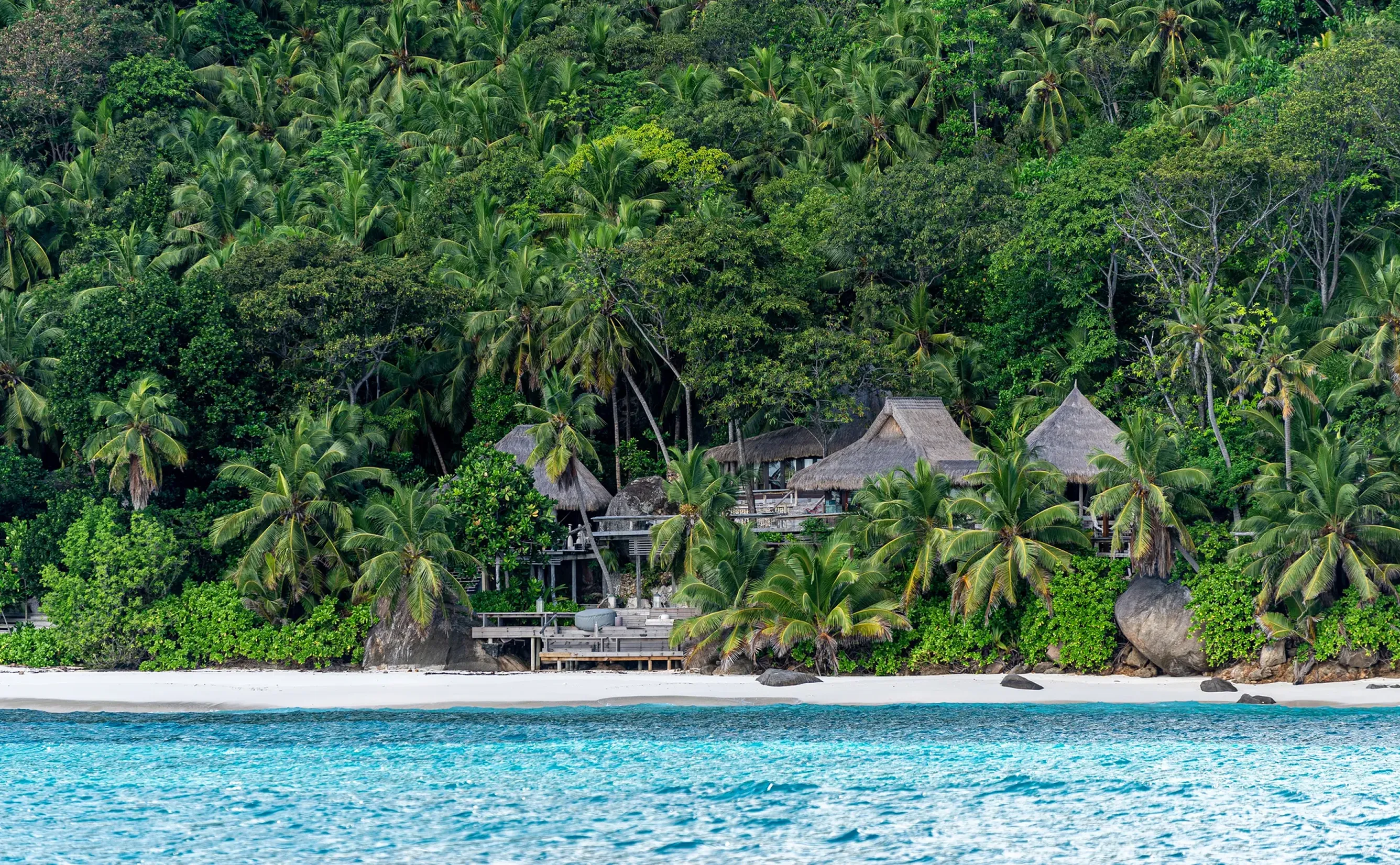 Secluded thatched beach bungalows by turquoise sea